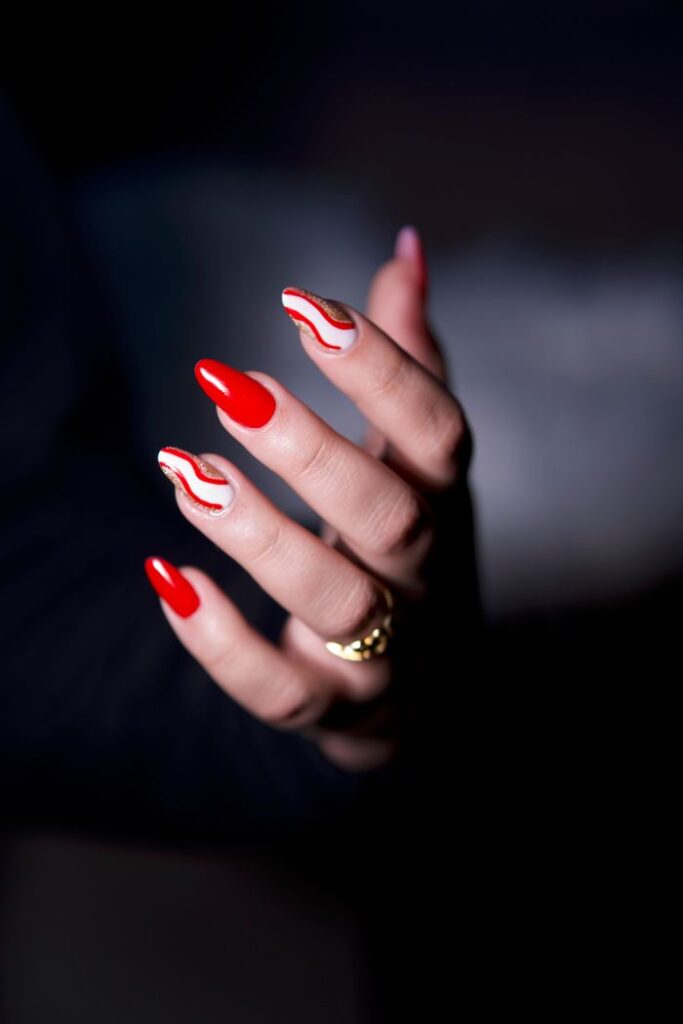 A close-up of a hand with elegant red and white nail art, showcasing stylish design.